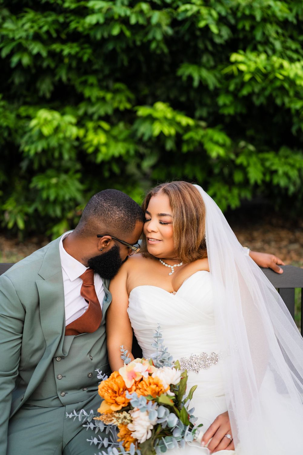Tender wedding portrait of newlyweds sitting together with orange and white floral bouquet.