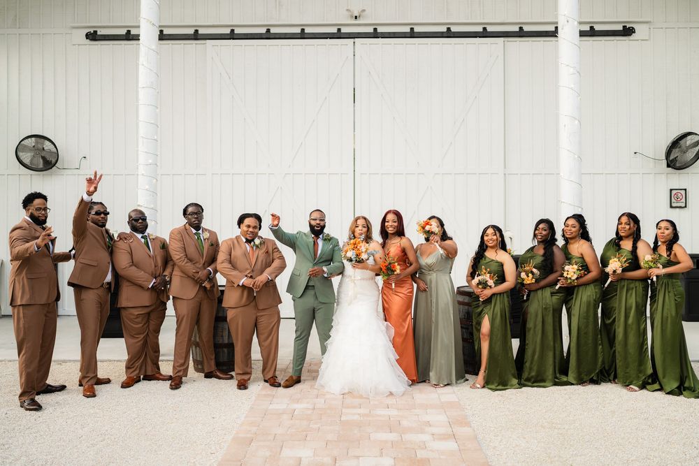 Wedding party in earth tones and olive green attire poses together against white wall at modern venue.