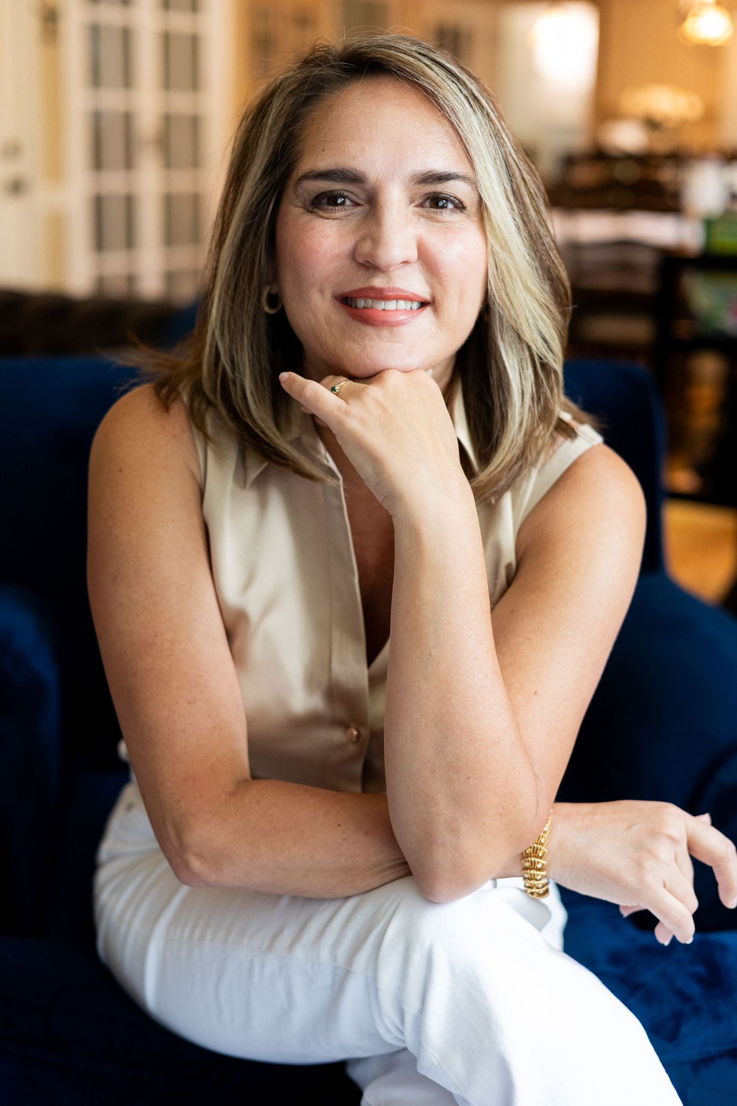 Professional woman in sleeveless white top sitting relaxed on blue couch.