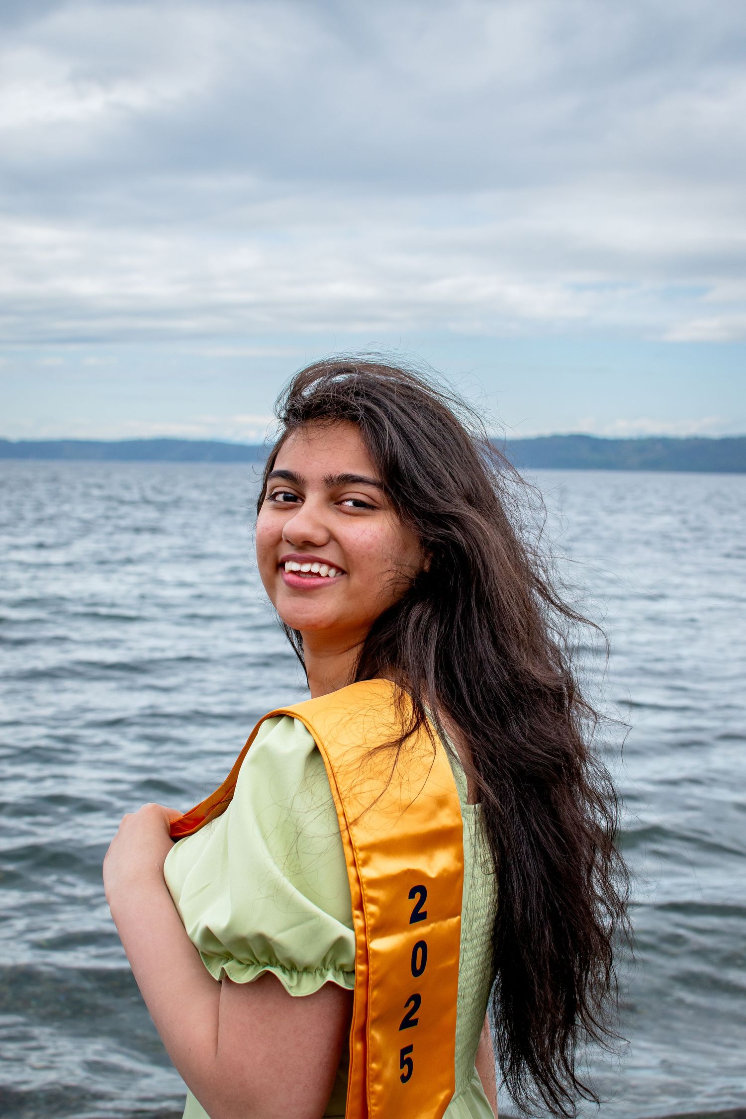 Confident senior in cap and gown smiling by the water graduation portraits with a fresh, coastal feel in Federal Way, WA.