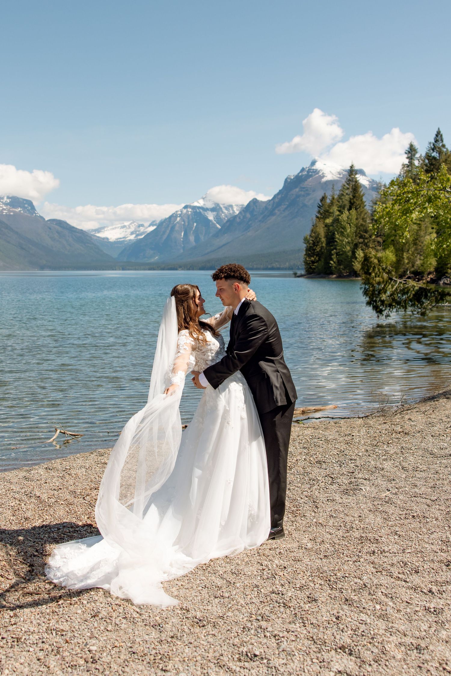 A couple in wedding attire share an intimate moment on a rocky riverbank during autumn in the mountains.