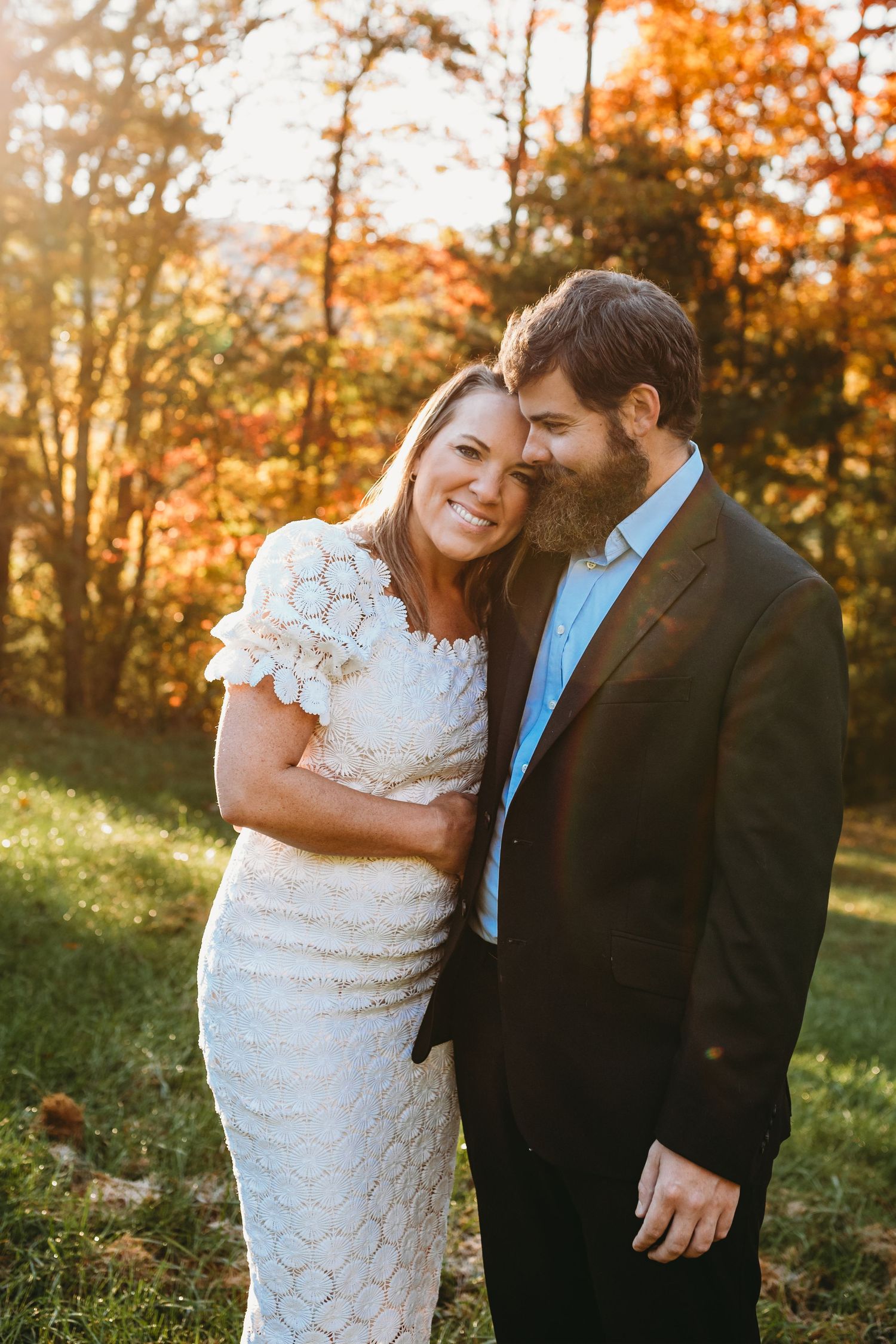A loving couple shares an intimate moment amid autumn trees with warm sunlight filtering through.