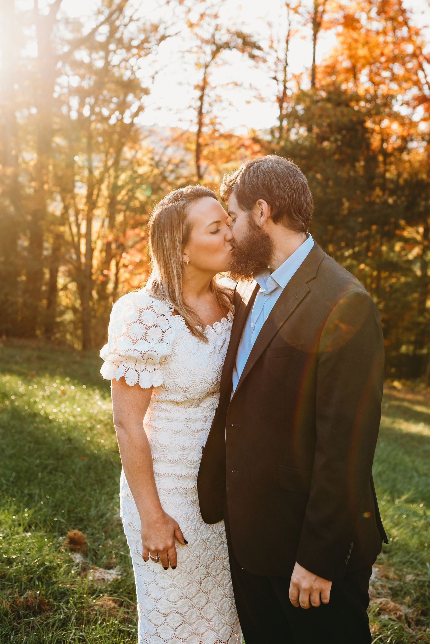A romantic moment between a couple in formal attire against a backdrop of fall foliage.