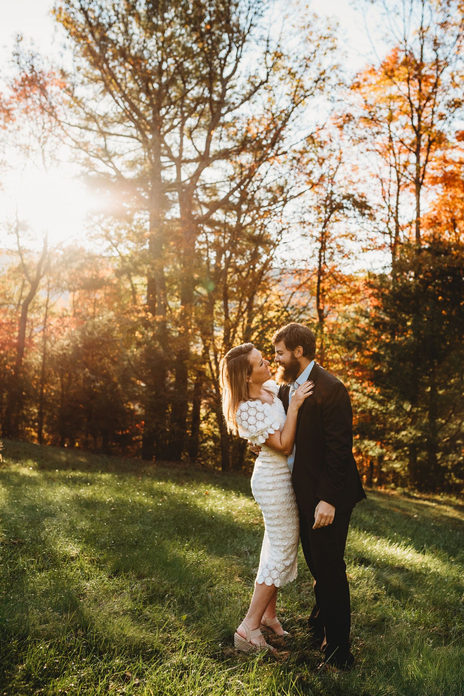 A romantic couple embraces in a sunlit autumn forest setting with golden foliage.