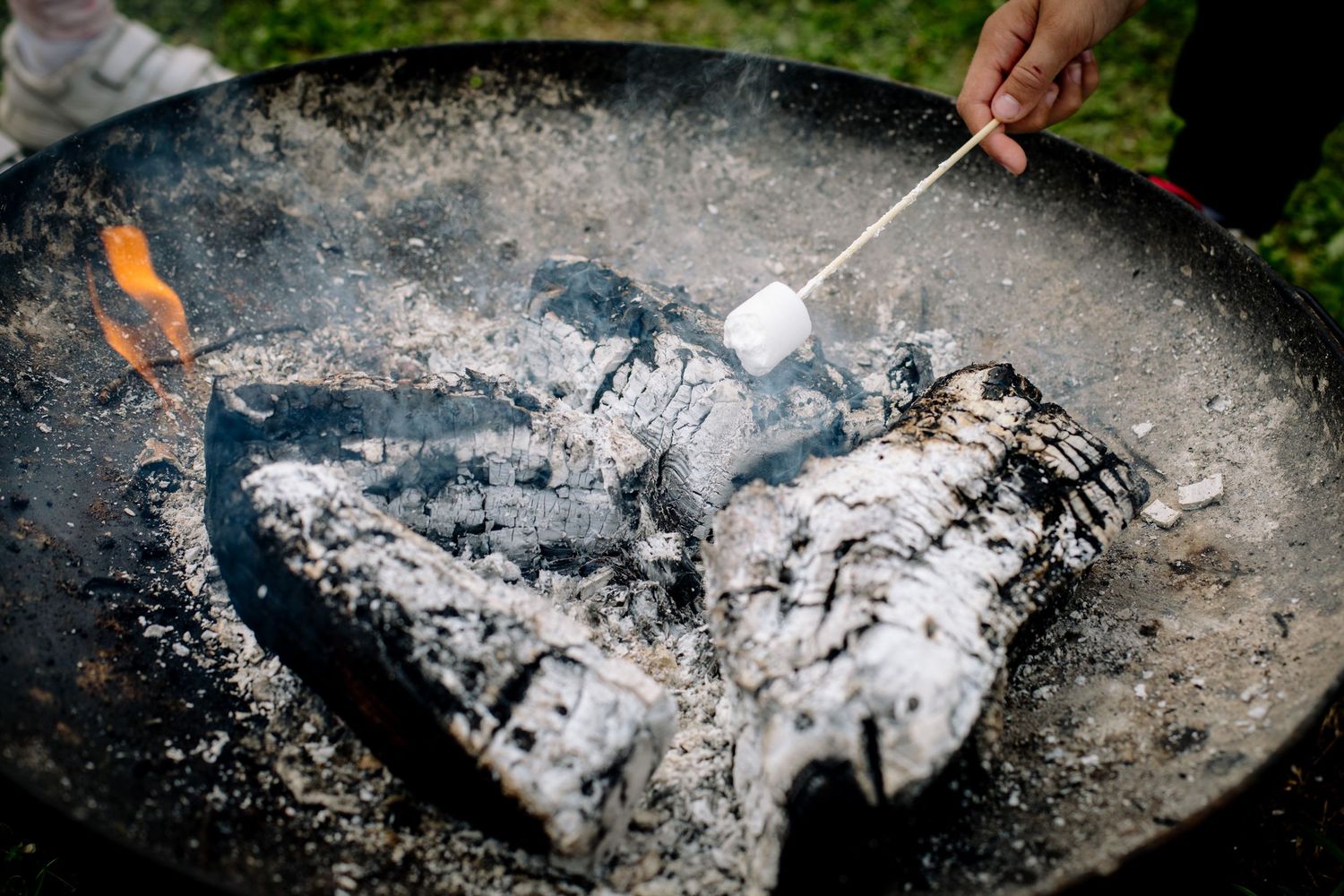 A white marshmallow being roasted over hot coals in a fire pit with glowing embers.