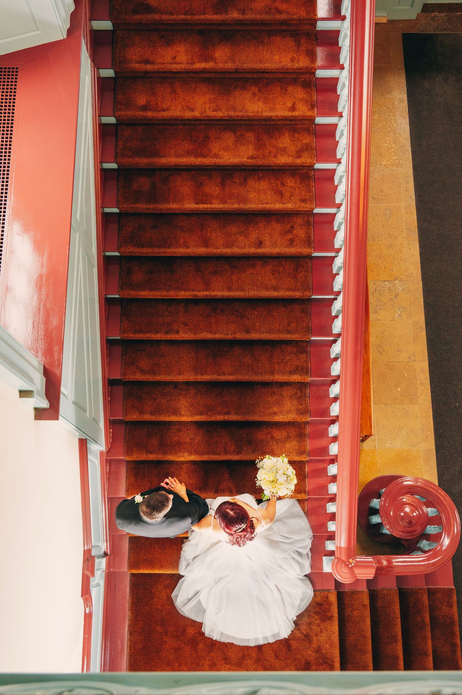 Overhead view of a red carpeted staircase with someone in a white dress descending the steps.