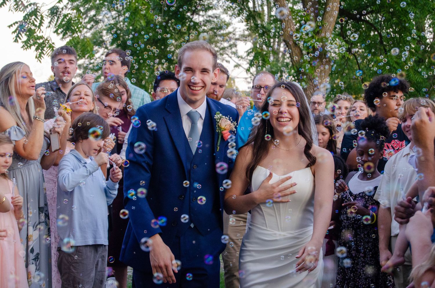 A happy couple celebrates at their outdoor wedding ceremony while guests blow bubbles around them in a joyful moment.