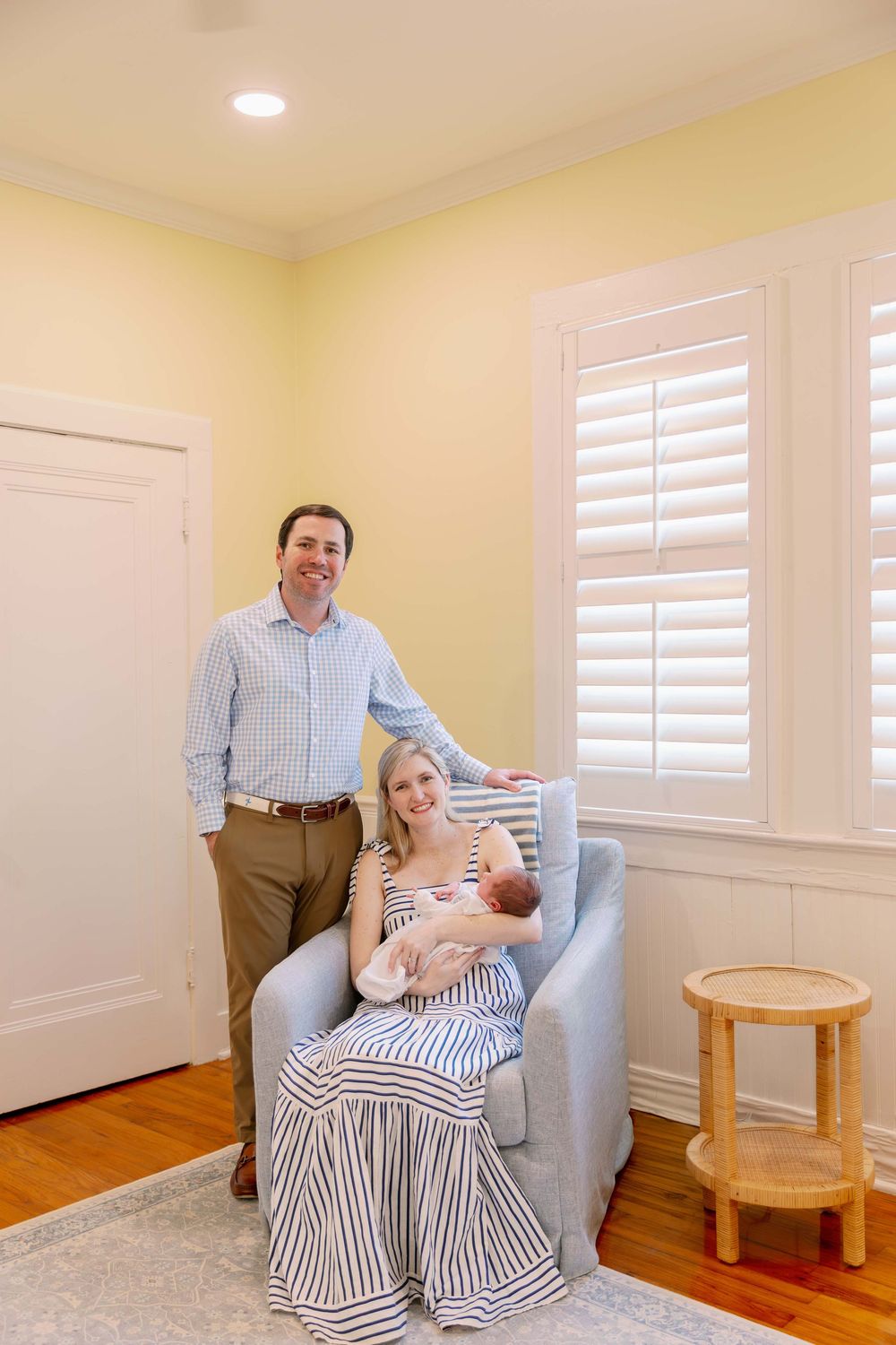 A cozy nursery scene featuring a light gray armchair, white plantation shutters and warm yellow walls.