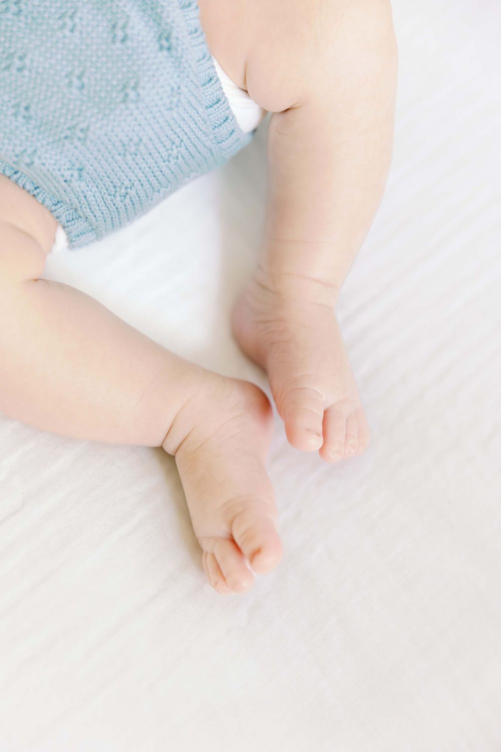 Tiny baby feet wearing soft knit blue booties on white bedding.