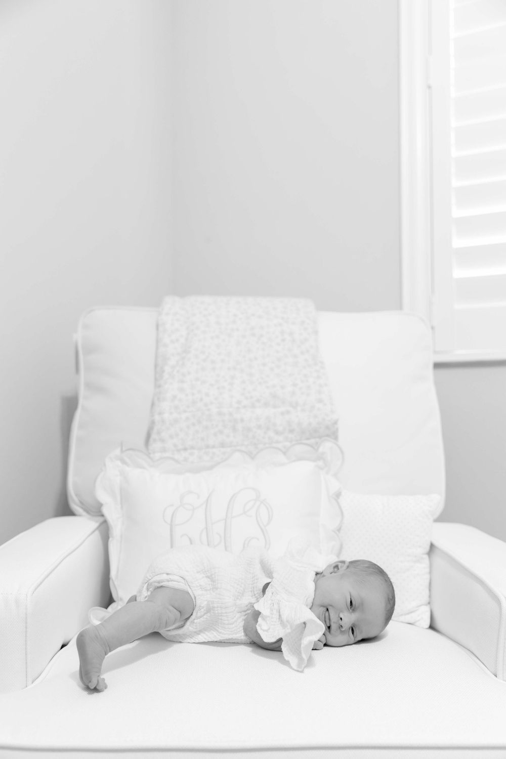 Sleeping baby in white dress lying on decorative white pillow in a cozy armchair.