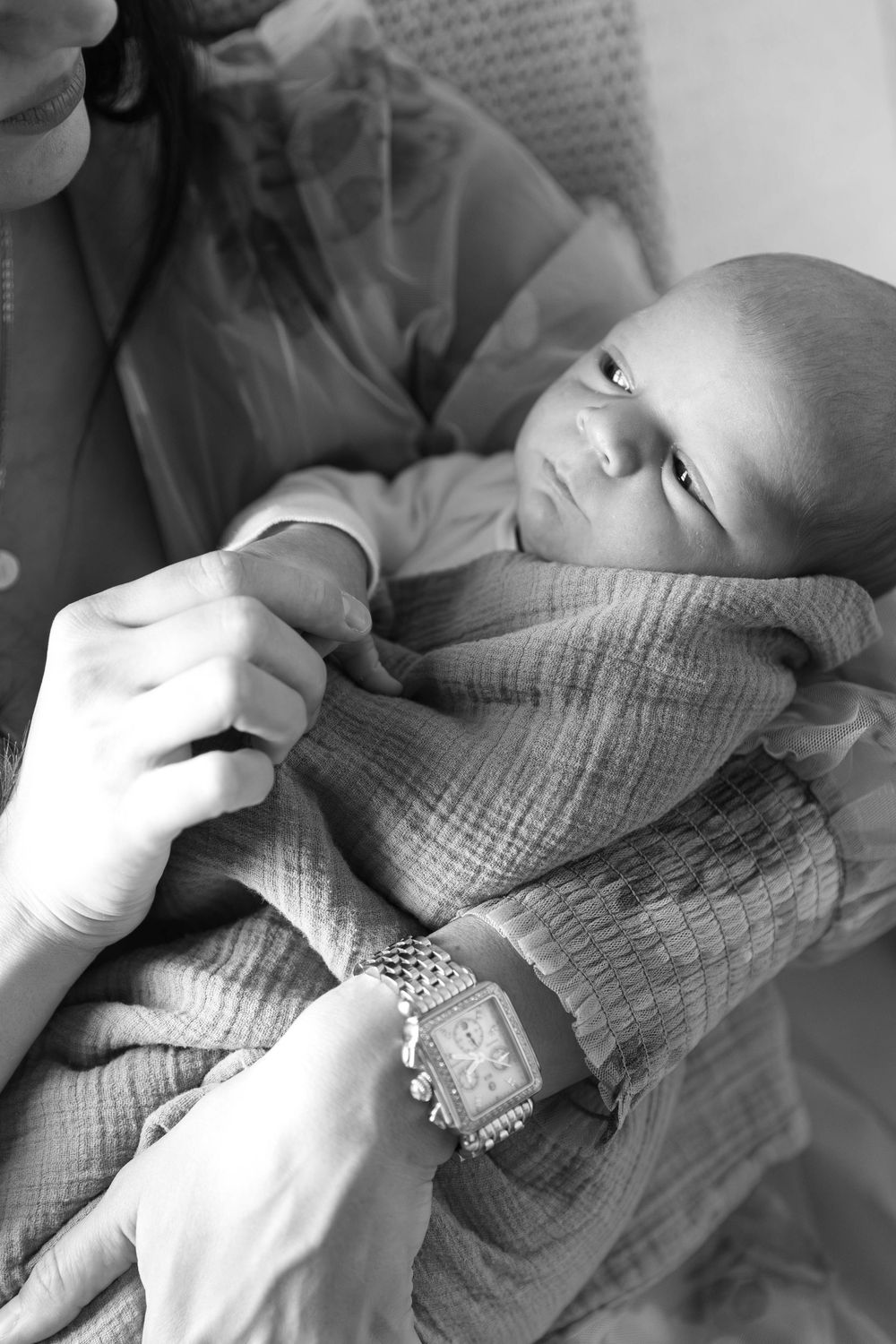 A black and white photograph of an infant wrapped in a textured blanket with hands gently holding them.
