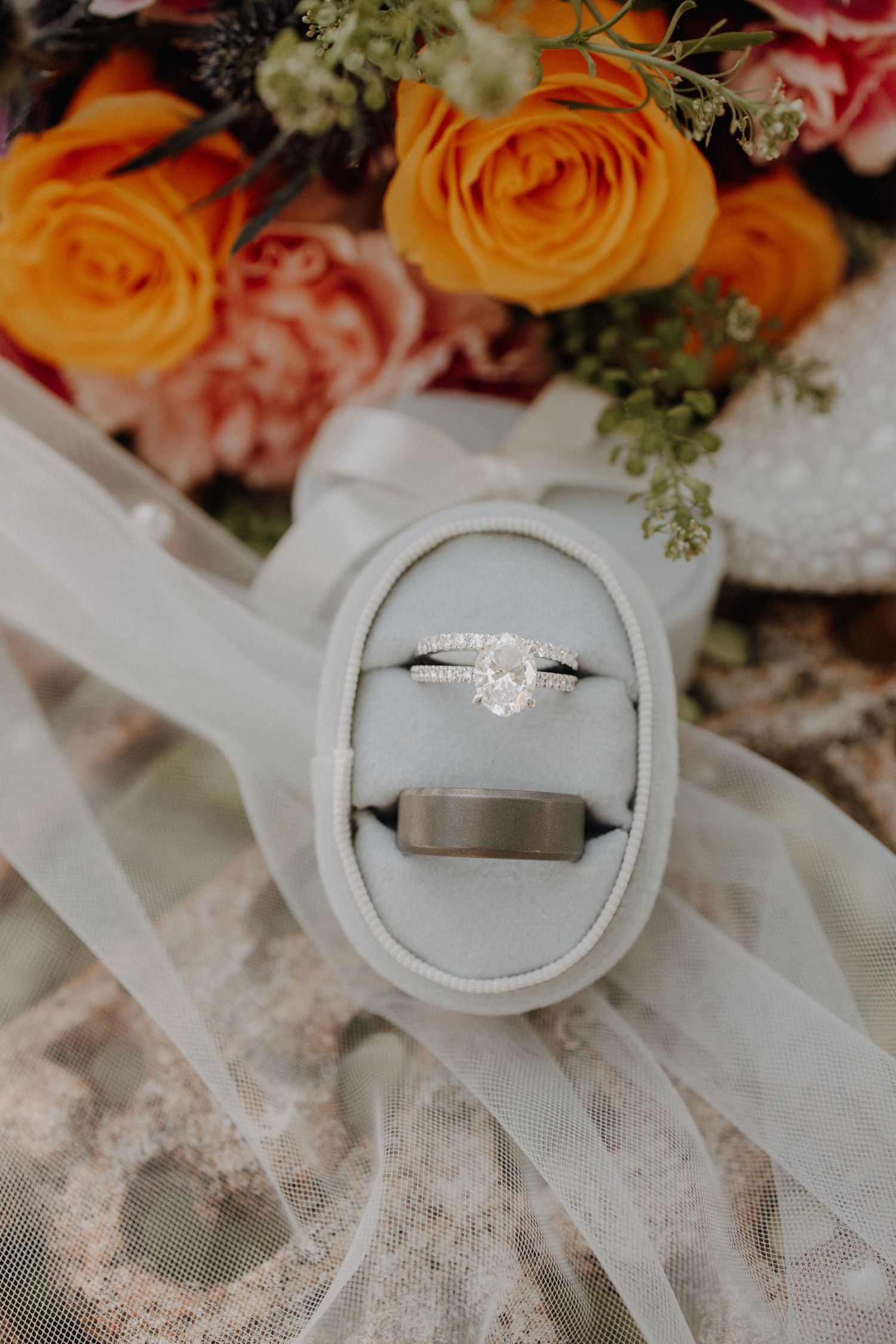 Diamond engagement ring and wedding bands displayed on white lace with orange roses.