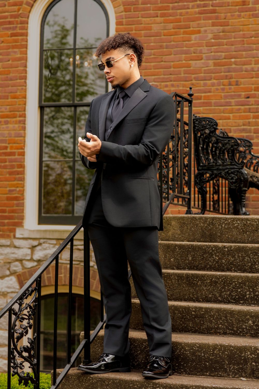 Stylish person in black suit checking phone on ornate stone steps.