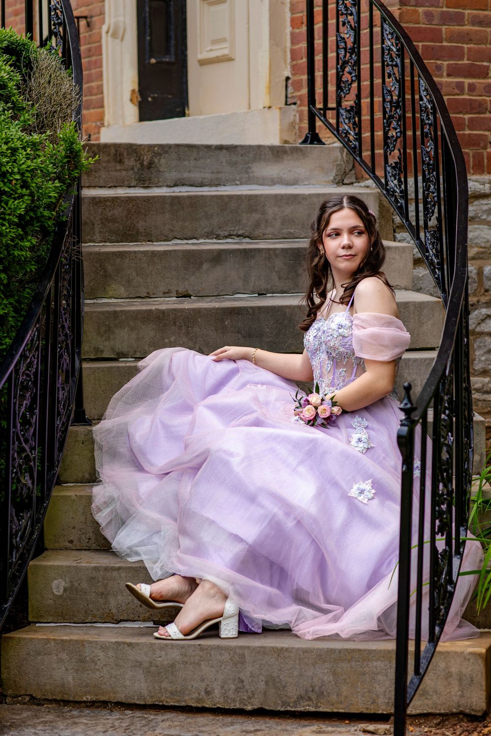 Person in purple formal gown seated elegantly on stone steps with iron railing.