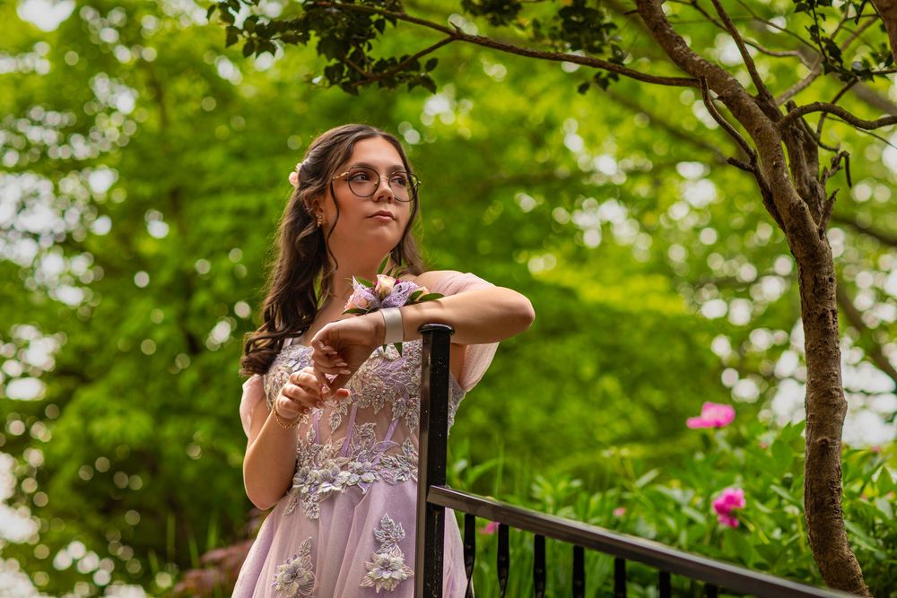 Romantic portrait of someone in a lavender formal dress posing on an ornate balcony with greenery.