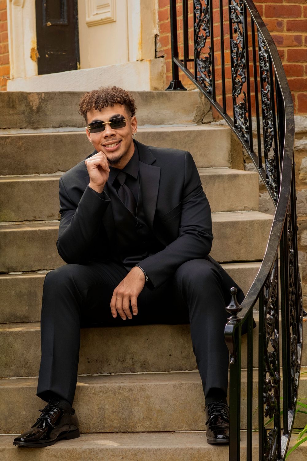 Fashionable portrait sitting on stone steps wearing sunglasses and all black attire.