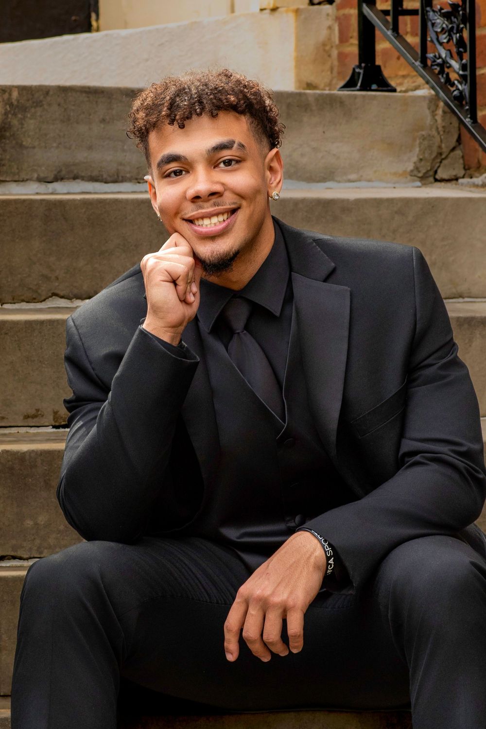 Professional portrait in black suit sitting casually on stone steps.