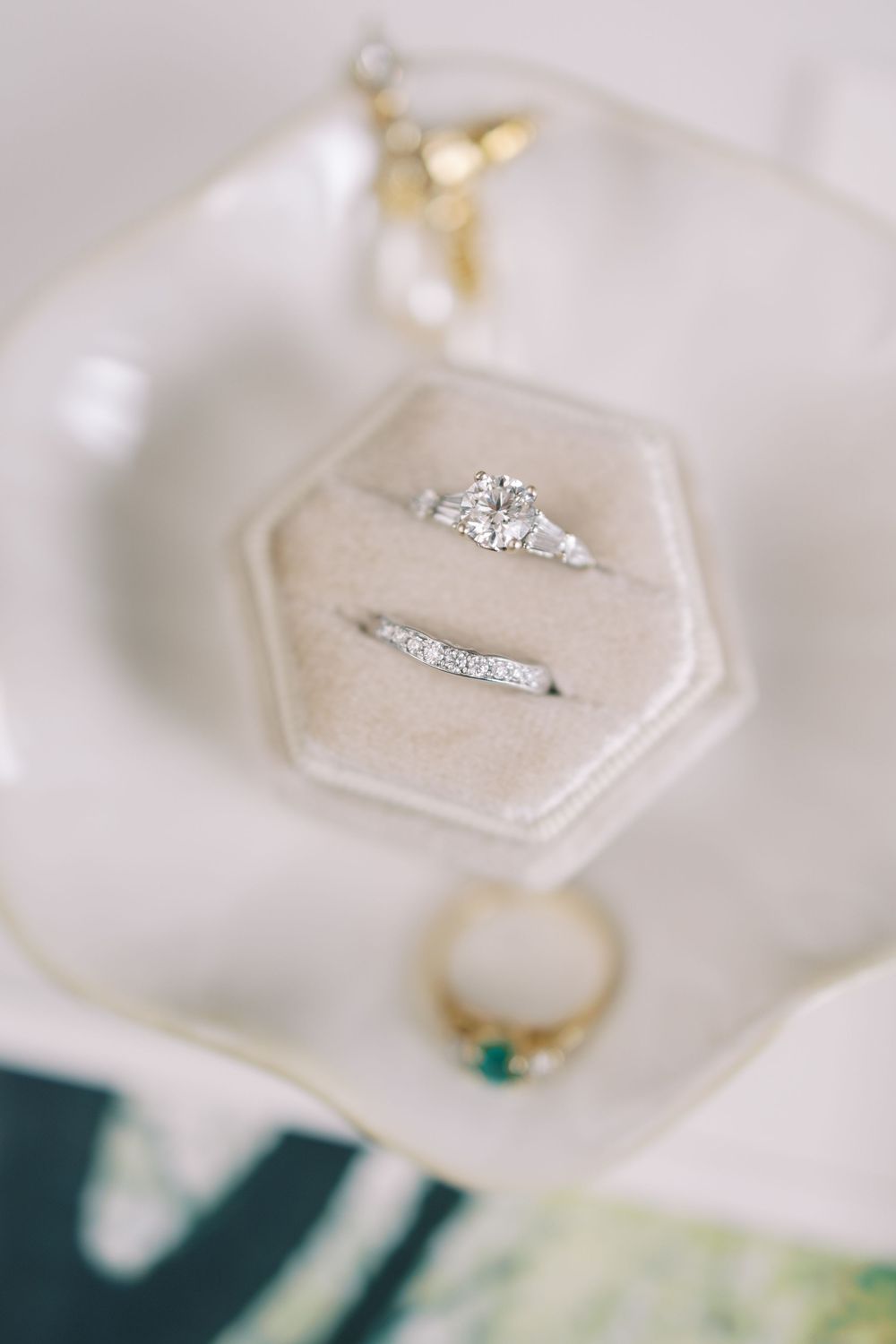 A delicate engagement ring and wedding band set displayed in a cream-colored hexagonal ring box on a white surface at Hall of Springs.