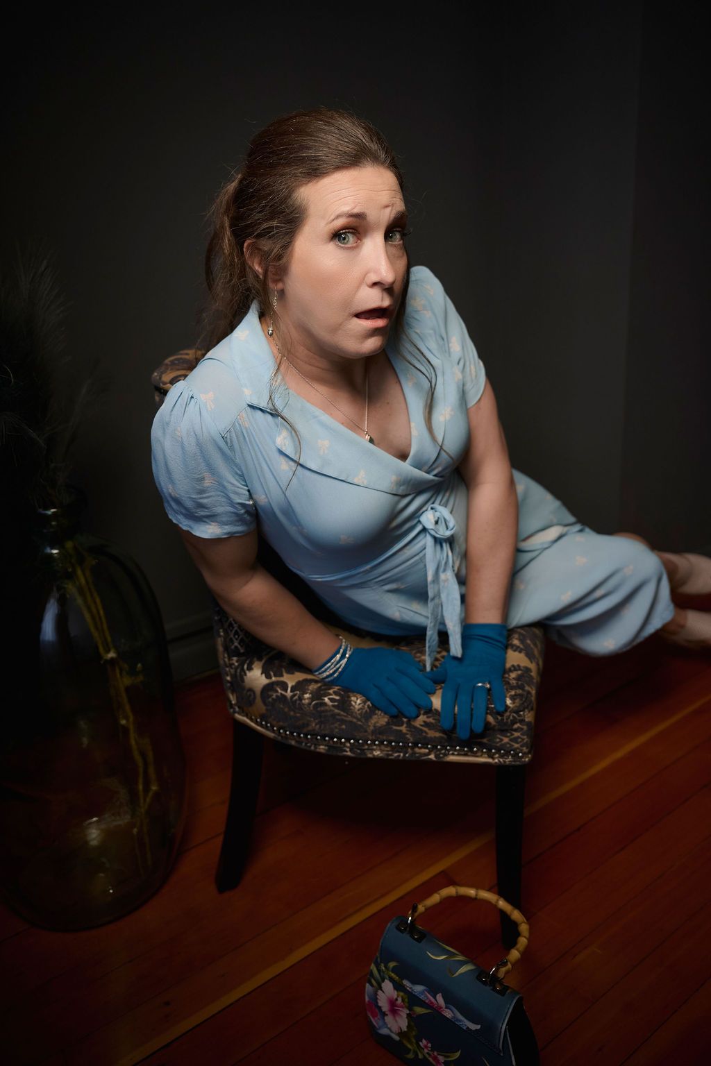 A retro styled portrait of someone in a light blue vintage dress sitting on an ornate chair against a dark background.
