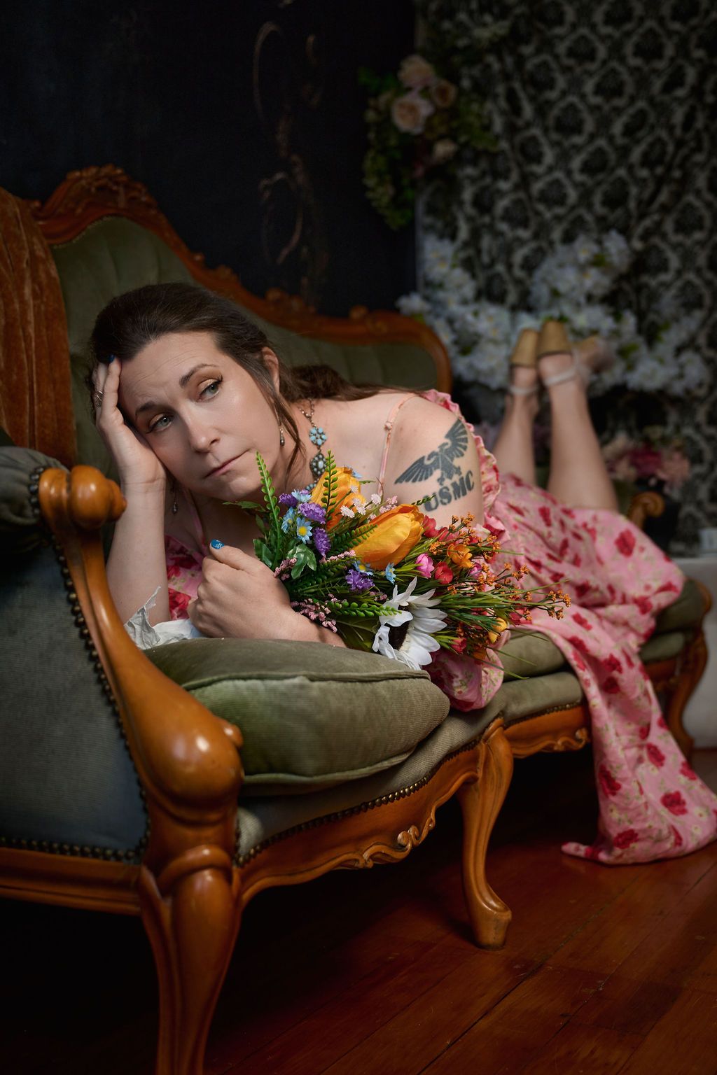 A moody portrait on an antique chaise lounge with colorful flowers and patterned background decor.