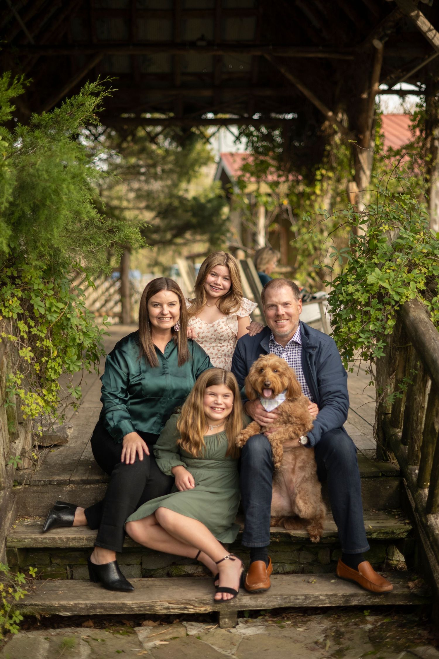 Family sits together on rustic wooden bench with their goldendoodle dog in Leiper's Fork.