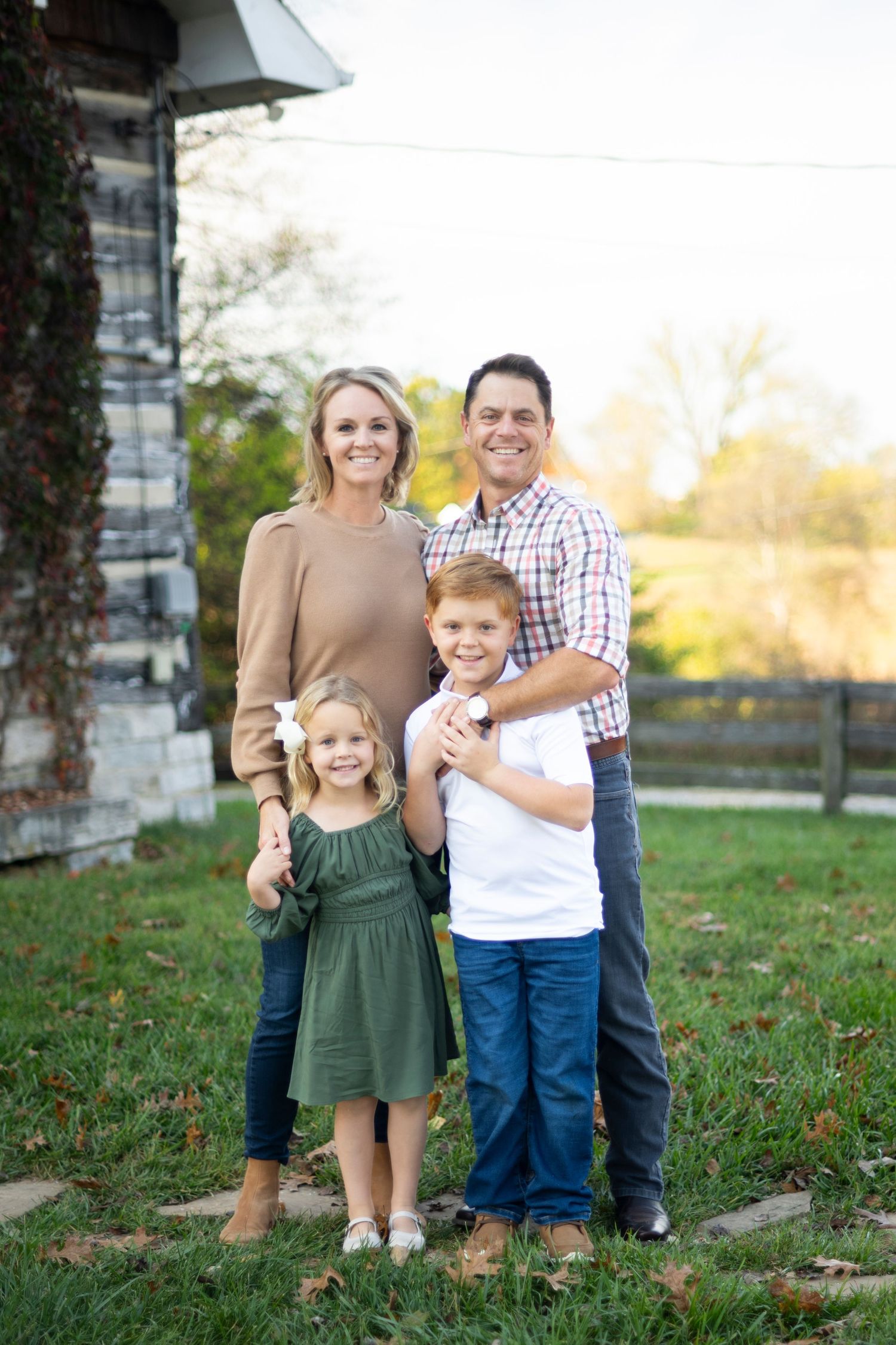 Family of four posing together outdoors near an ivy-covered stone building in autumn in Columbia, TN.