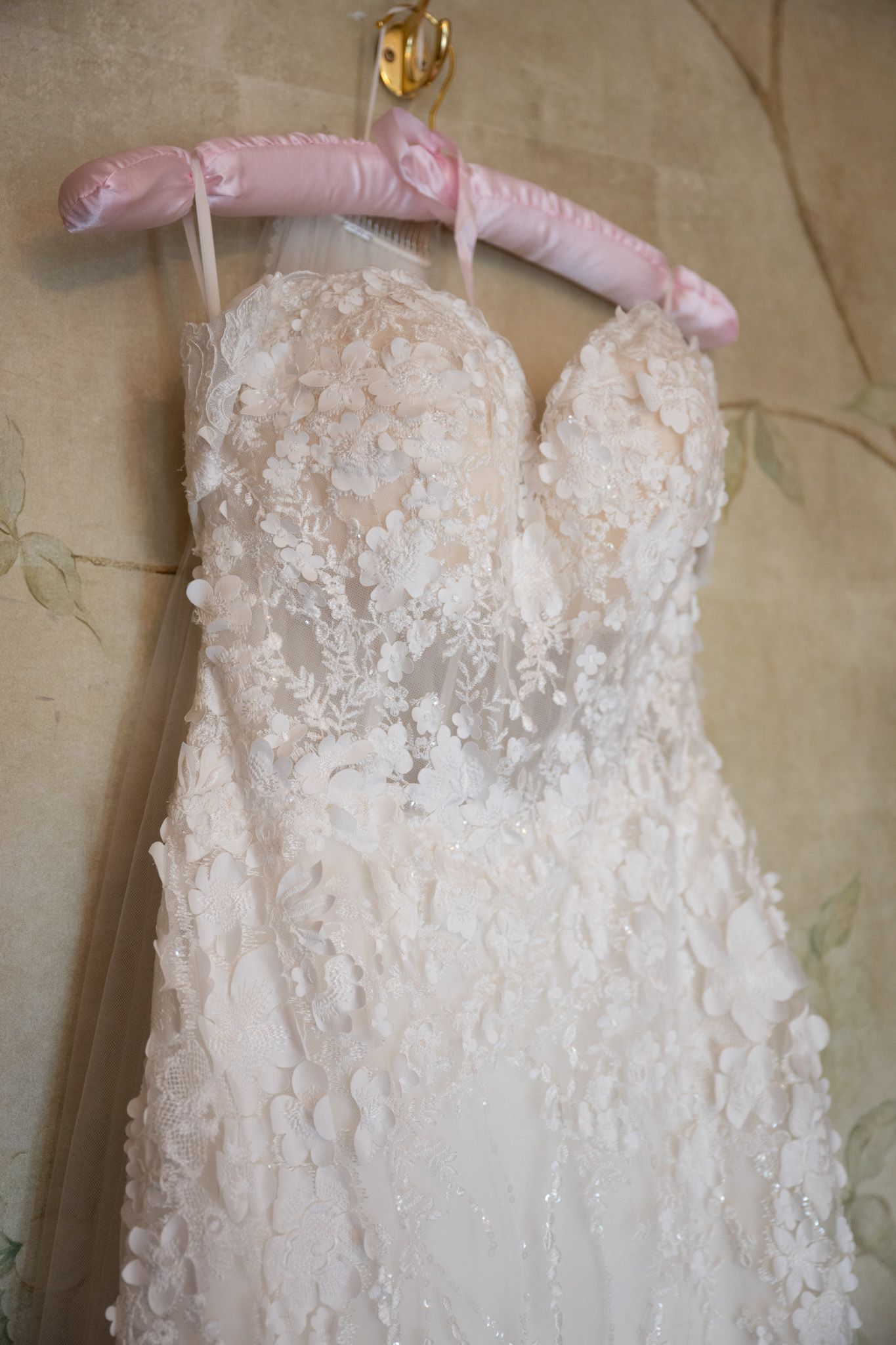 Close-up details of delicate white lace appliques and beadwork on a wedding dress hanging on a pink hanger.