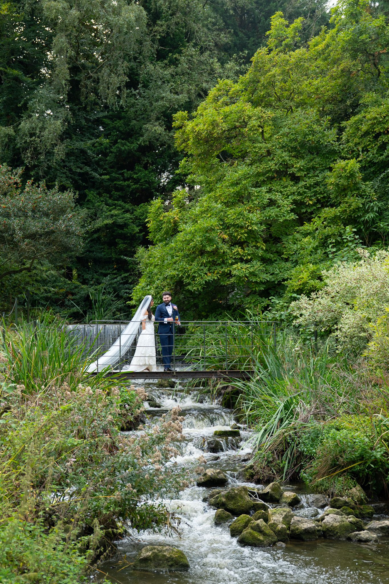 A cascading stream flows through a lush green garden with stone steps and natural landscaping creating a peaceful waterfall scene.