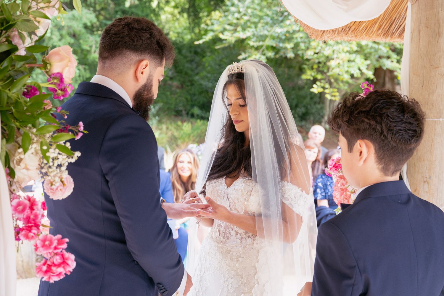 An intimate wedding ceremony moment under a floral-decorated gazebo with attendees in formal attire.