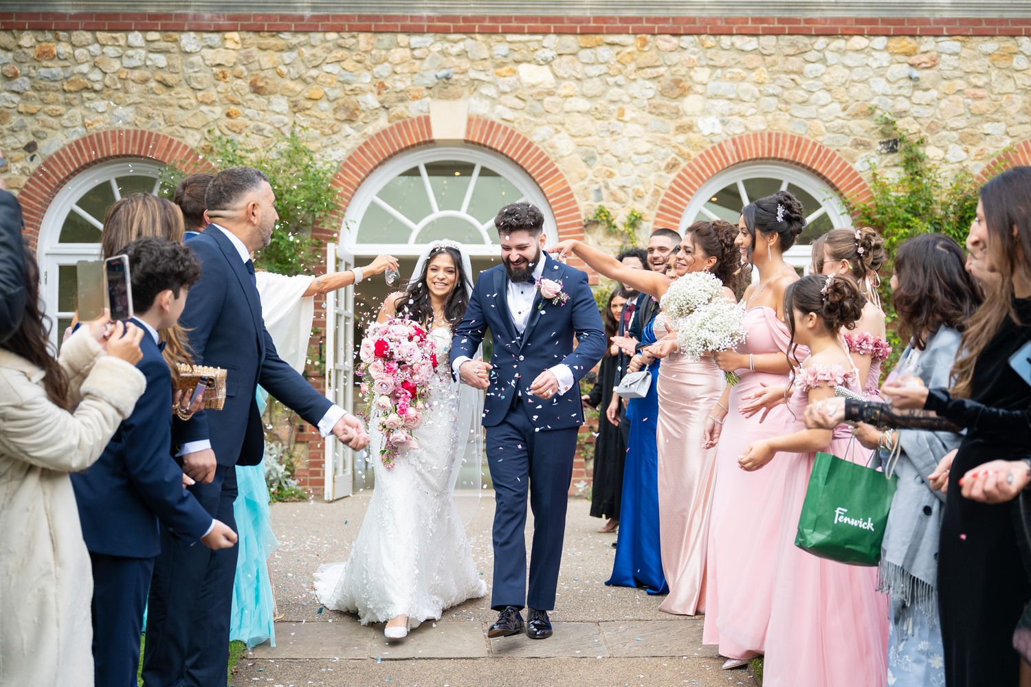 Wedding guests line up outside a rustic stone building to shower newlyweds with confetti during their exit celebration.