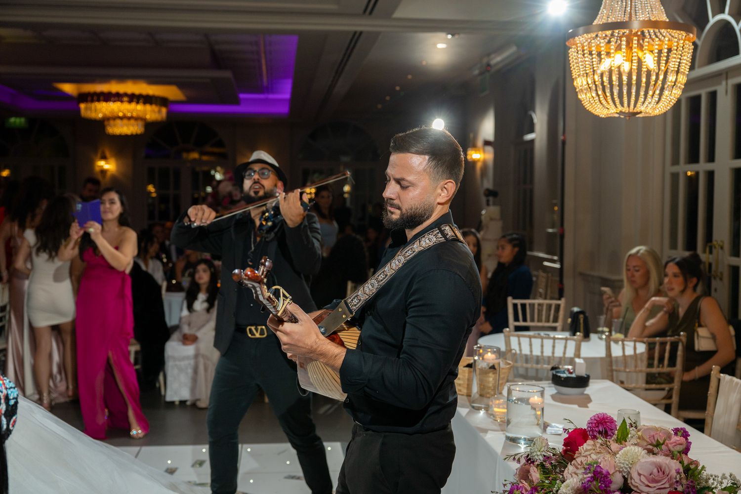 Wedding guests dance and celebrate on the dance floor under elegant chandeliers at an evening reception.