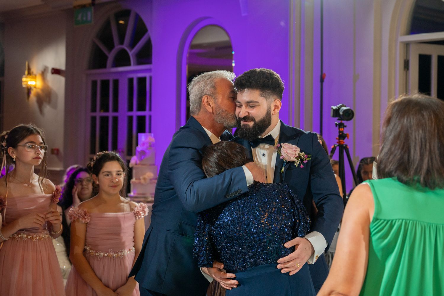 People dancing and celebrating at an elegant indoor event with purple lighting and formal attire.