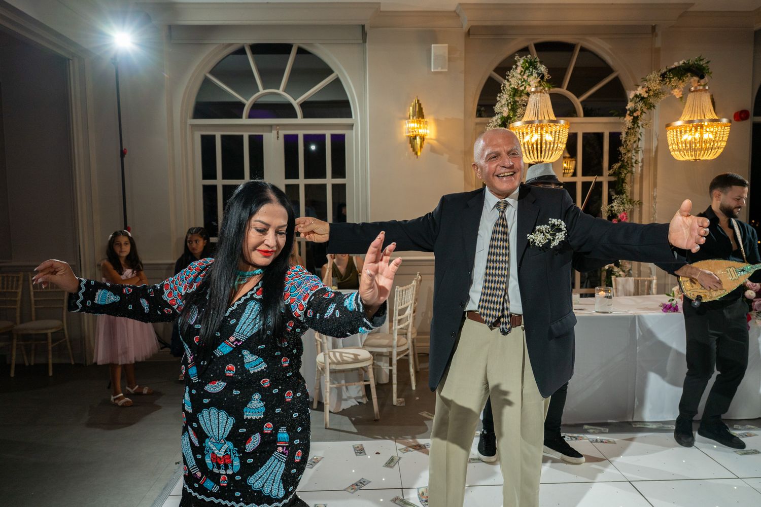 People dancing and celebrating at an elegant indoor reception with arched windows and warm lighting.