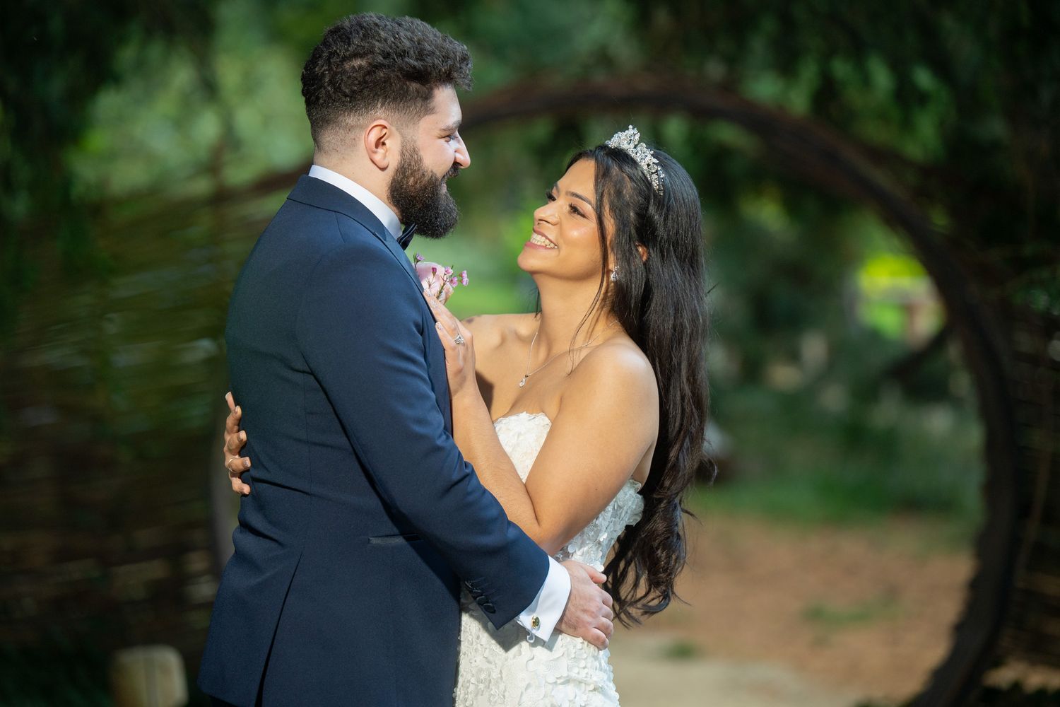 Romantic wedding couple embraces outdoors in a garden setting with natural greenery in the background.