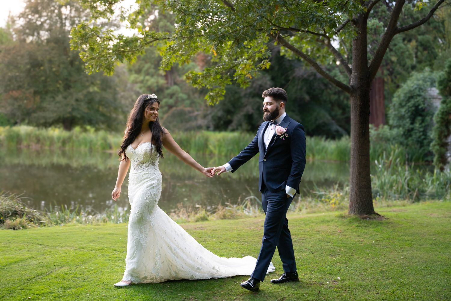 A couple dances together on a lush green lawn surrounded by trees during a romantic outdoor photoshoot.