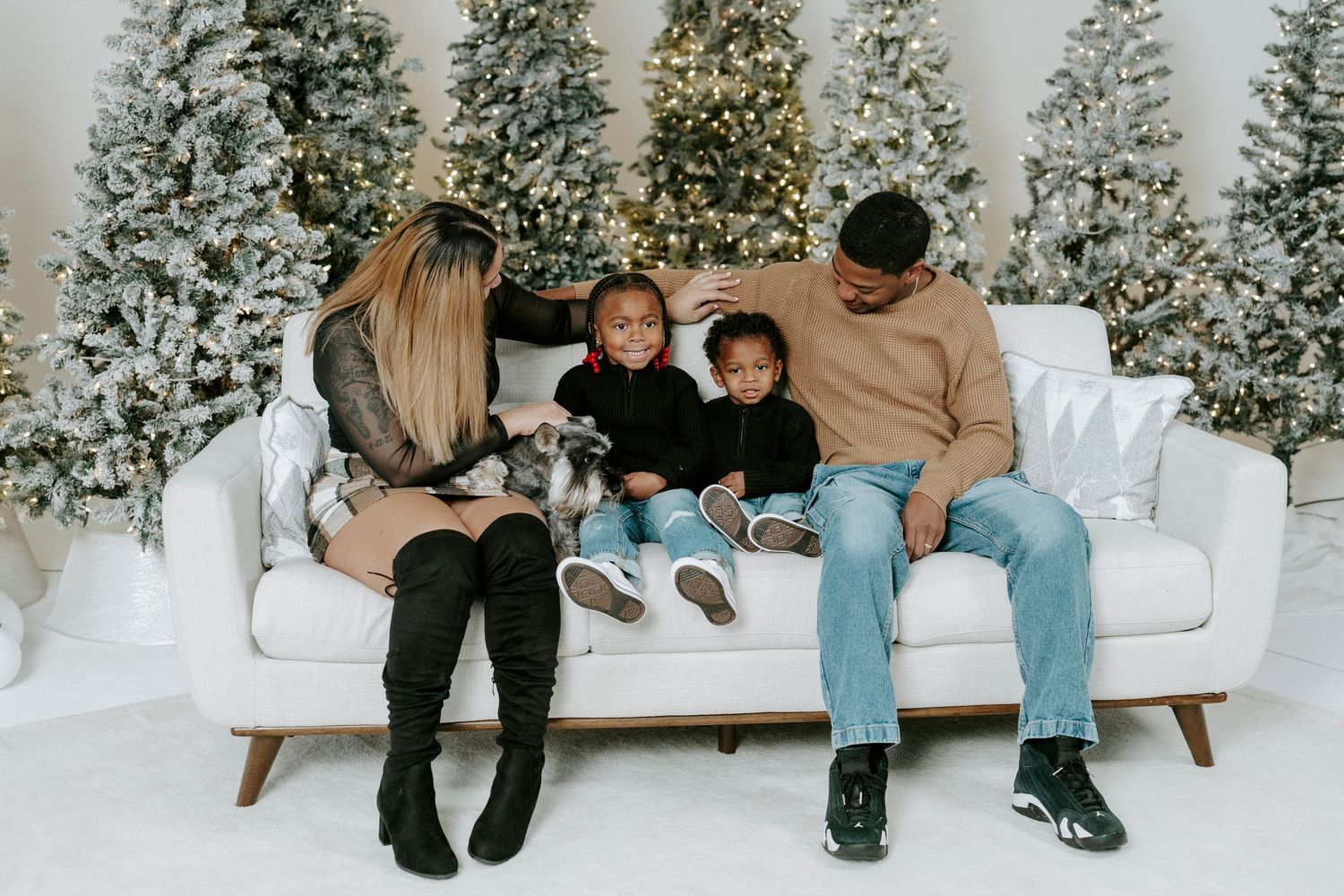 People sitting together on a white couch in front of snowy evergreen trees during winter.