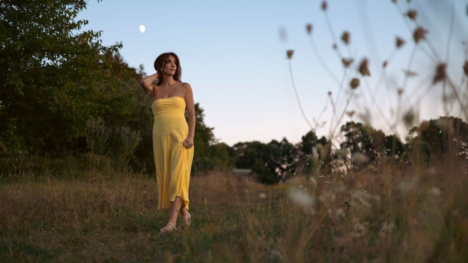 A person in a yellow dress stands in a field at sunset creating a dreamy silhouette against the golden sky.