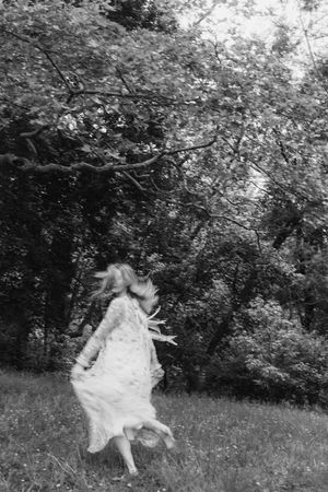 A series of black and white photos showing someone twirling in a dress in a meadow with trees in the background.