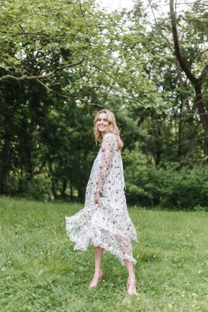 A person wearing a delicate floral dress dances gracefully through a green summer meadow.