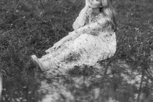 Monochrome photograph of a person lying in a grassy field with wildflowers in a dreamy pose.