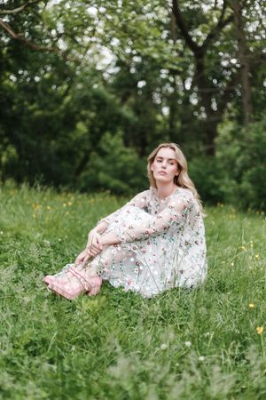 A dreamy outdoor portrait showing someone lying in tall grass wearing a delicate floral dress.
