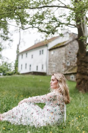 A floral dress flows in the breeze as someone reclines on a grassy hillside near stone buildings.