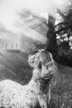 Black and white portrait of someone lying in tall grass with dreamy sunlit bokeh effects.