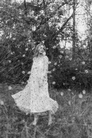 Artistic black and white photo showing a flowing white dress against dark foliage with ethereal light effects.