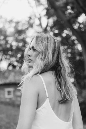 Black and white portrait showing the back profile view of someone with wavy hair wearing a white dress.
