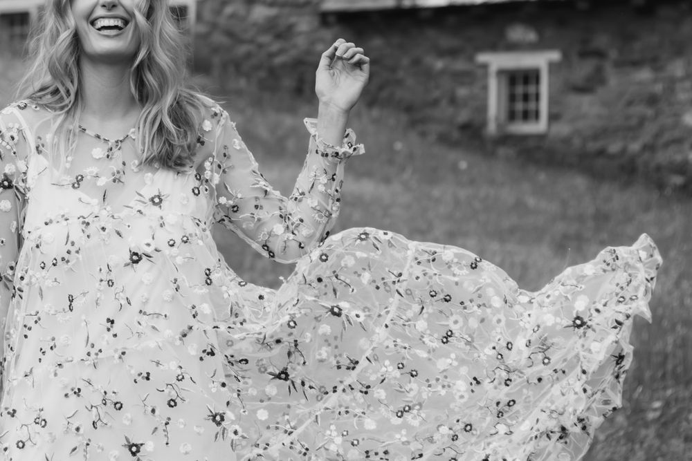 A person in a flowing floral dress twirls joyfully in a black and white outdoor portrait.