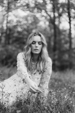 Black and white photo of a person lying in a wildflower meadow wearing a light colored dress.