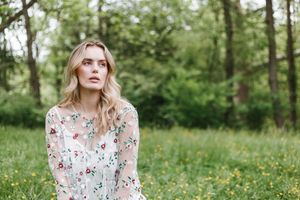 A person in a floral dress stands in a lush green meadow with wildflowers on a sunny spring day.