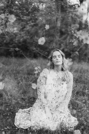 A dreamy black and white photo series shows a person in a floral dress sitting in a meadow with soft bokeh effects.