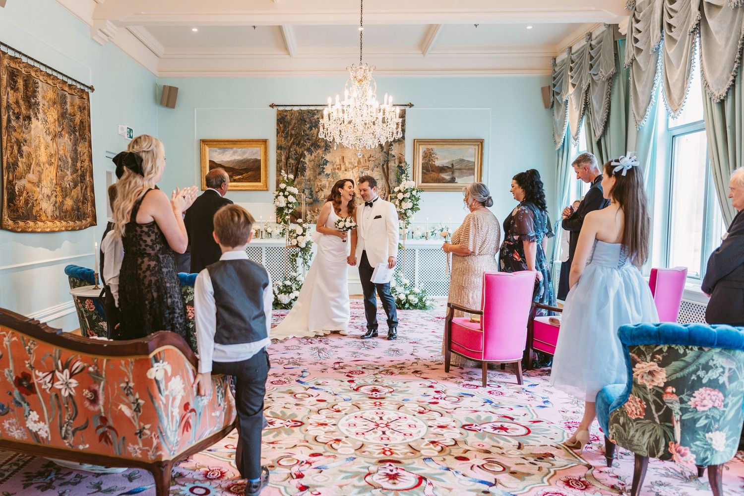 Wedding celebration in an elegant room with crystal chandelier and rose petals scattered across a patterned carpet.